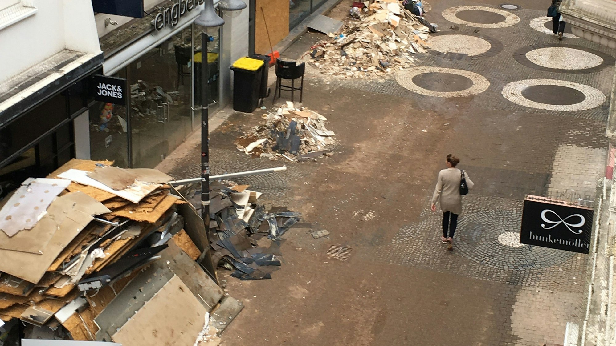 Das Bild zeigt die Neustraße, eine Passantin schaut auf Berge von Sperrmüll und Schutt.