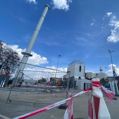 Zu sehen sind ein Schornstein und dahinter die weiteren Bauten des Eisenwerks.