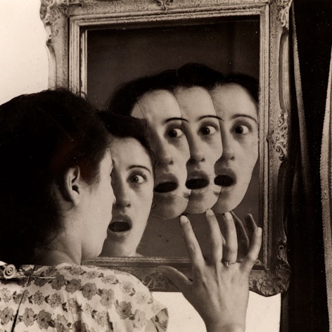 Eine Frau sieht mehrere Gesichter im Spiegel.