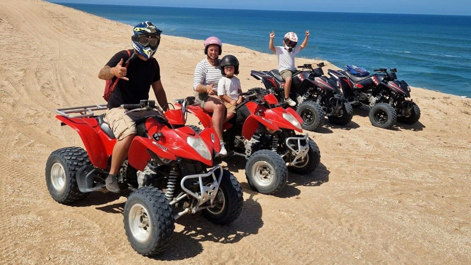 Eine Familie bei einer Quadtour durch Sanddünen.