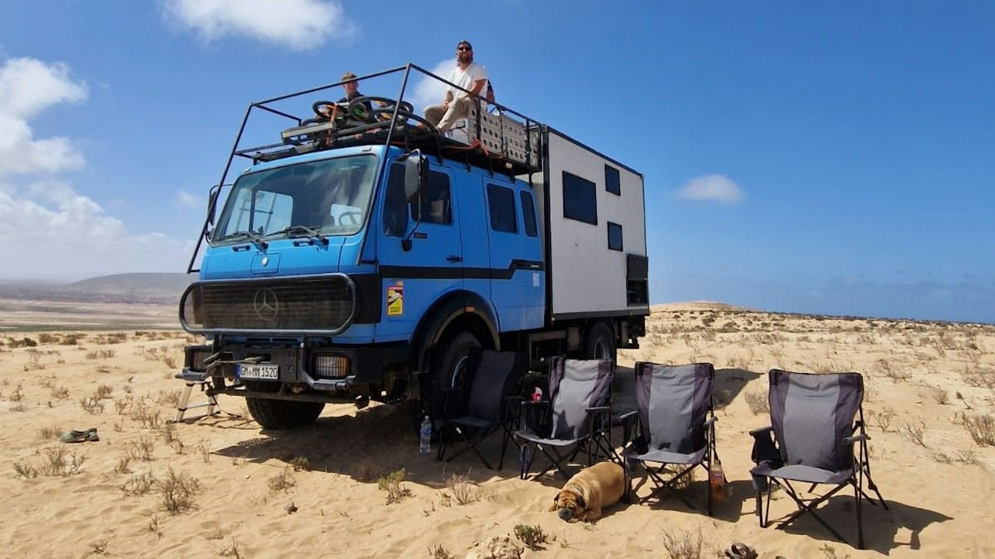 Ein hellblaues Expeditionsmobil parkt in einer wüstenähnlichen Landschaft