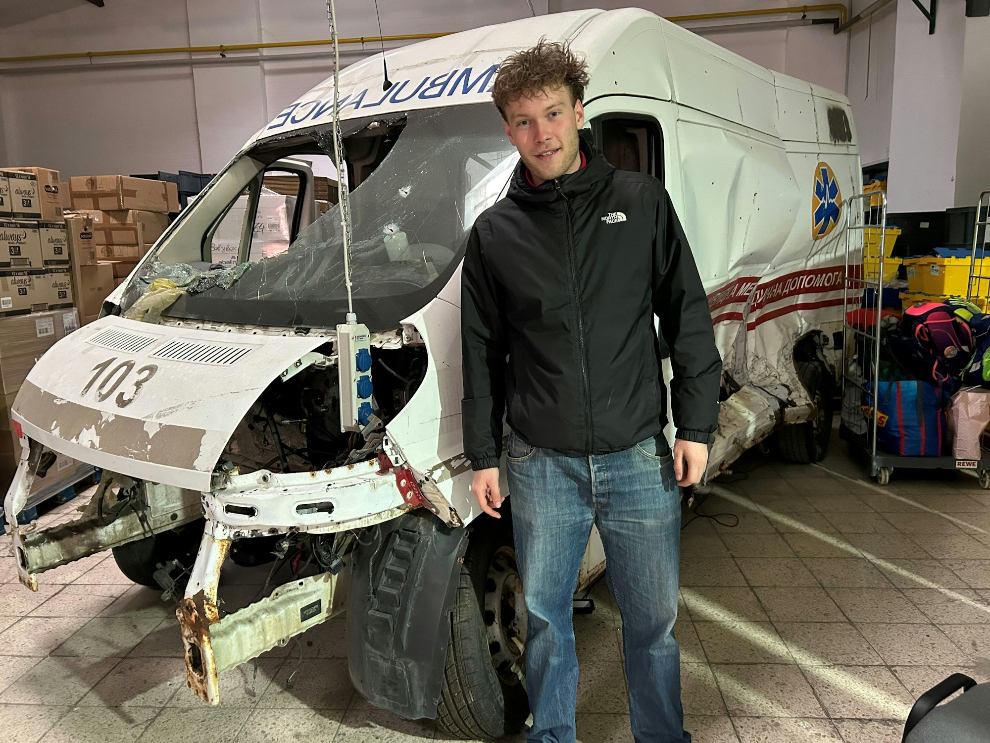 Lukas Inden steht der Halle vor einem bei einem russischen Angriff völlig zerstörten Krankenwagen.
