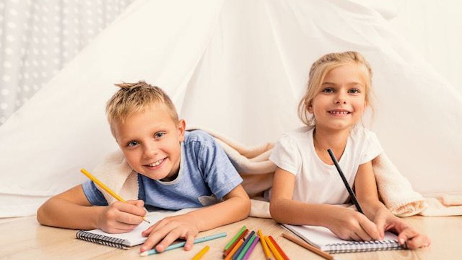 Zwei Kinder liegen auf dem Boden und haben Buntstifte in der Hand.