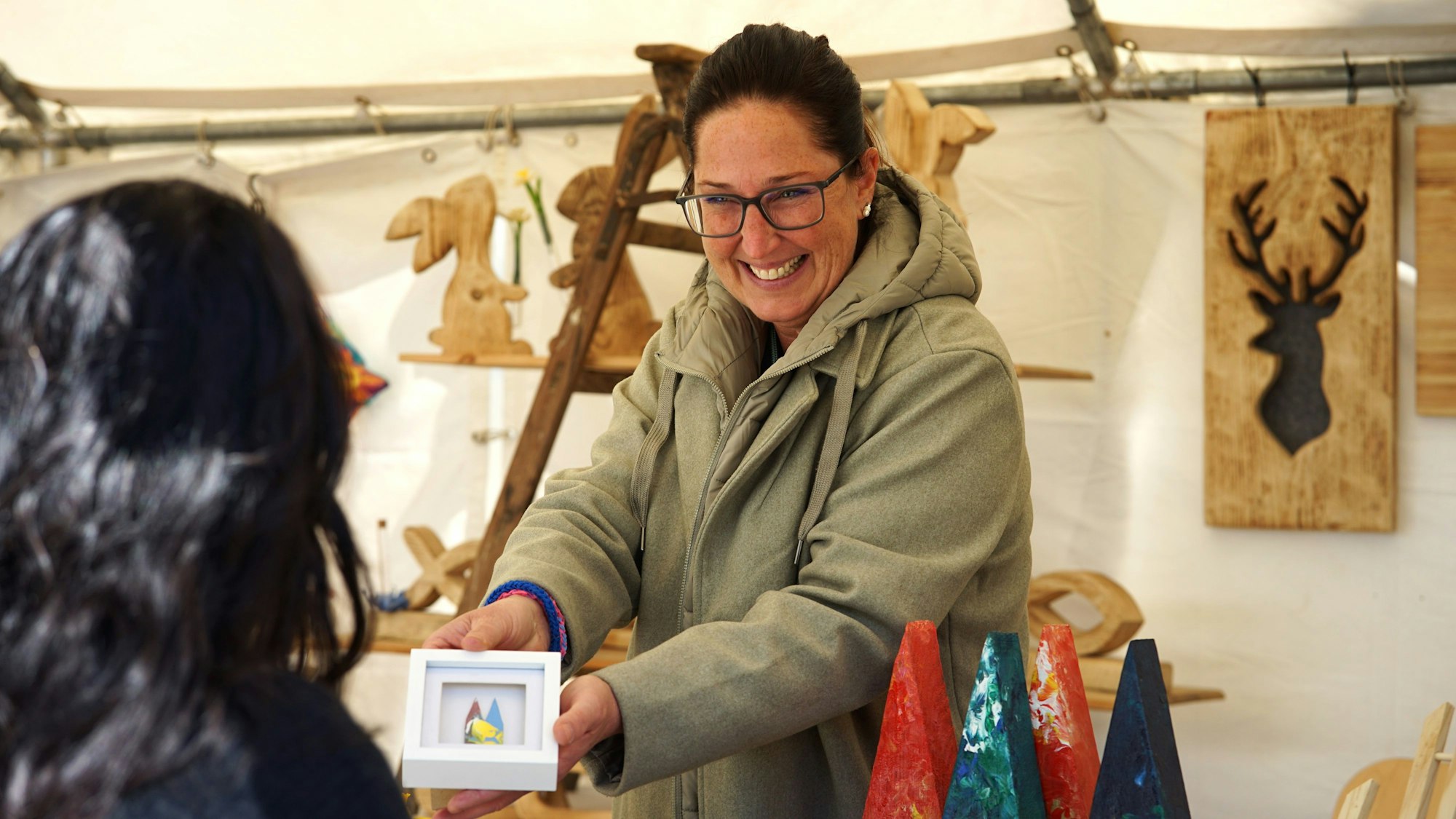 Zwei Frauen im Gespräch. Eine hält einen Rahmen in der Hand, darin ist der Kölner Dom zu sehen.
