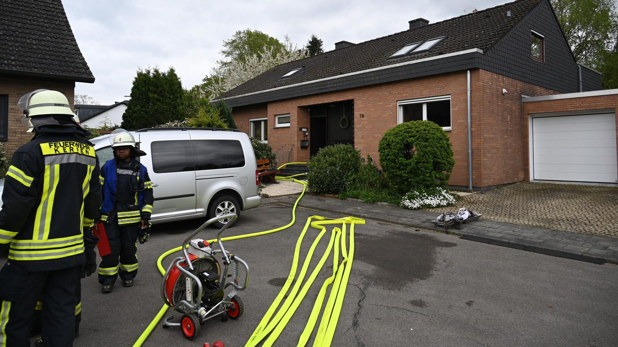 Auf dem Foto stehen Feuerwehrleute vor einem Haus. Auf dem Boden liegen gelbe Schlüche.