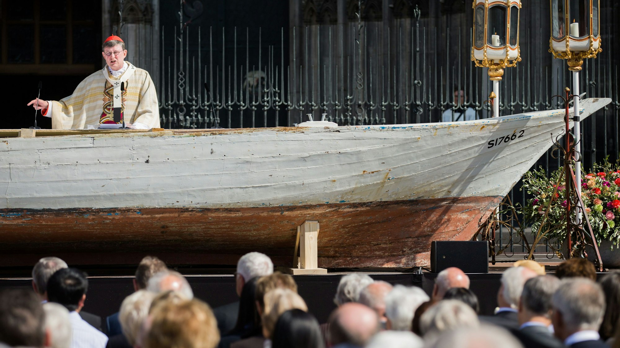 Kardinal Rainer Woelki fgestikuliert vor dem Kölner Dom an einem Flüchtlingsboot, das als Altar dient.