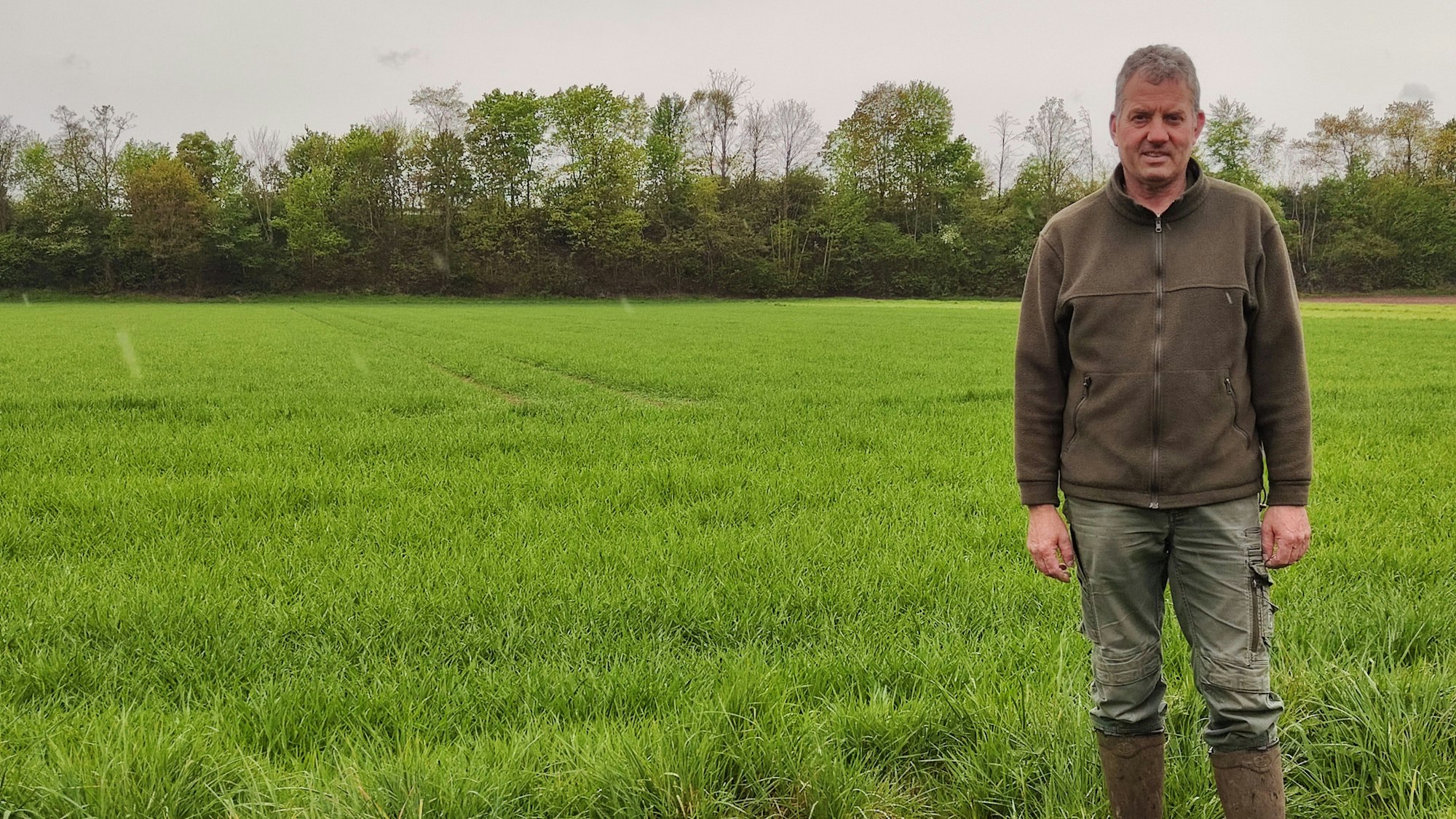 Bruno Lanzerath steht in Gummistiefel vor einer grünen Wiese. Im Hintergrund ist ein Baumstreifen zu sehen.