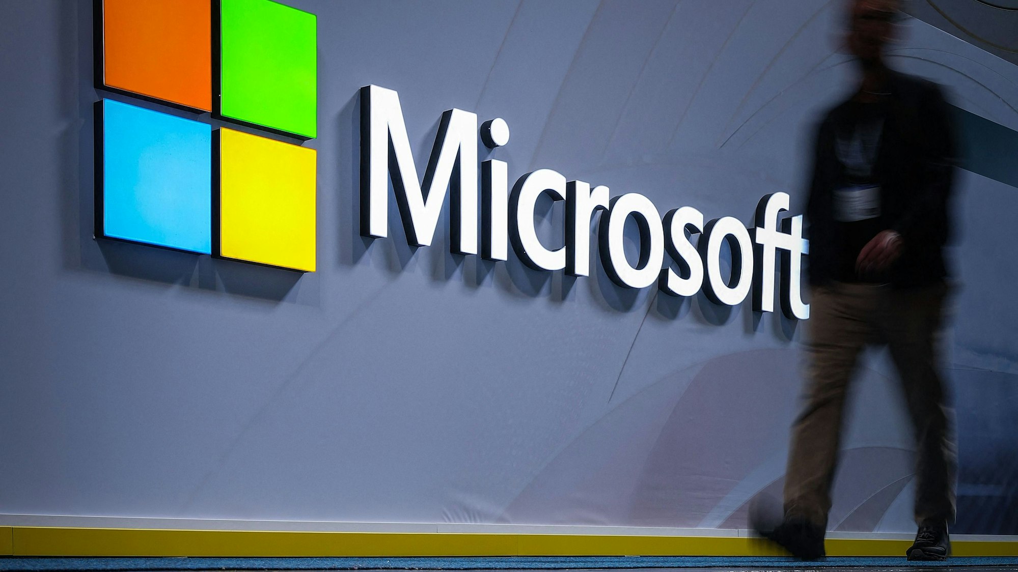 Ein Mann geht an einem Logo mit der Aufschrift Microsoft vorbei.