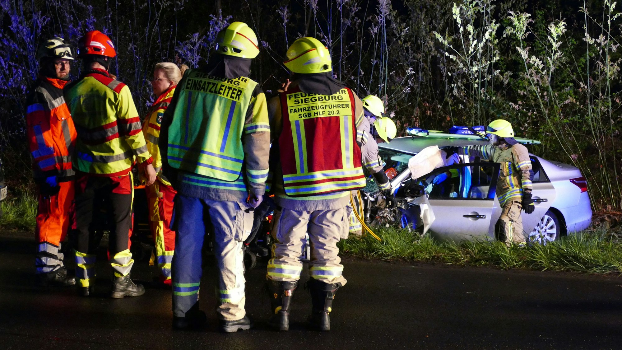 Feuerwehrleute stehen neben einem verunglückten Auto.