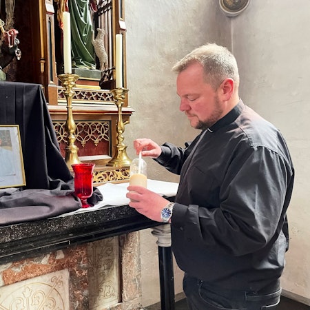Vor einem Bild des Papstes, das auf einem schwarzen Tuch aufgestellt wurde, entzündet der Pfarrer eine Kerze.