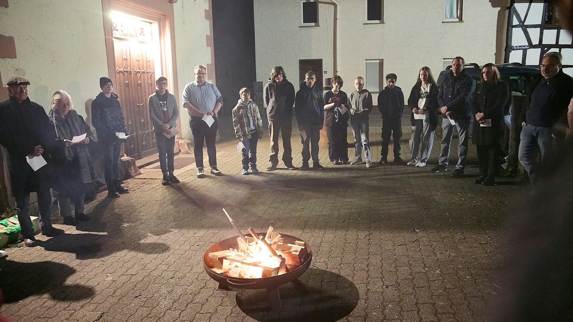 Die Teilnehmer haben sich in der Dunkelheit im Halbkreis um die Feuerschale versammelt.