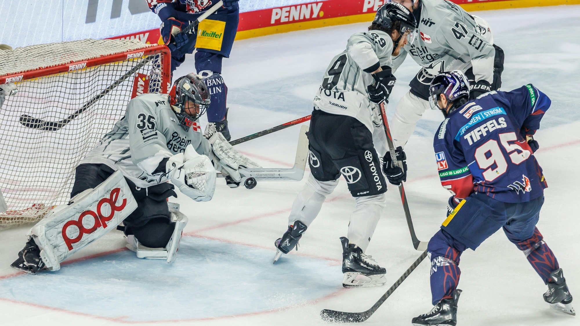 21.04.2025, Berlin: Eishockey: DEL, Eisbären Berlin - Kölner Haie, Meisterschaftsrunde, Finale, 3. Spieltag, Uber Arena. Torhüter Julius Hudacek (l-r), Gregor MacLeod und Veli-Matti Vittasmäki von Kölner Haie verteidigen das Tor gegen Berlins Frederik Tiffels. Foto: Andreas Gora/dpa +++ dpa-Bildfunk +++