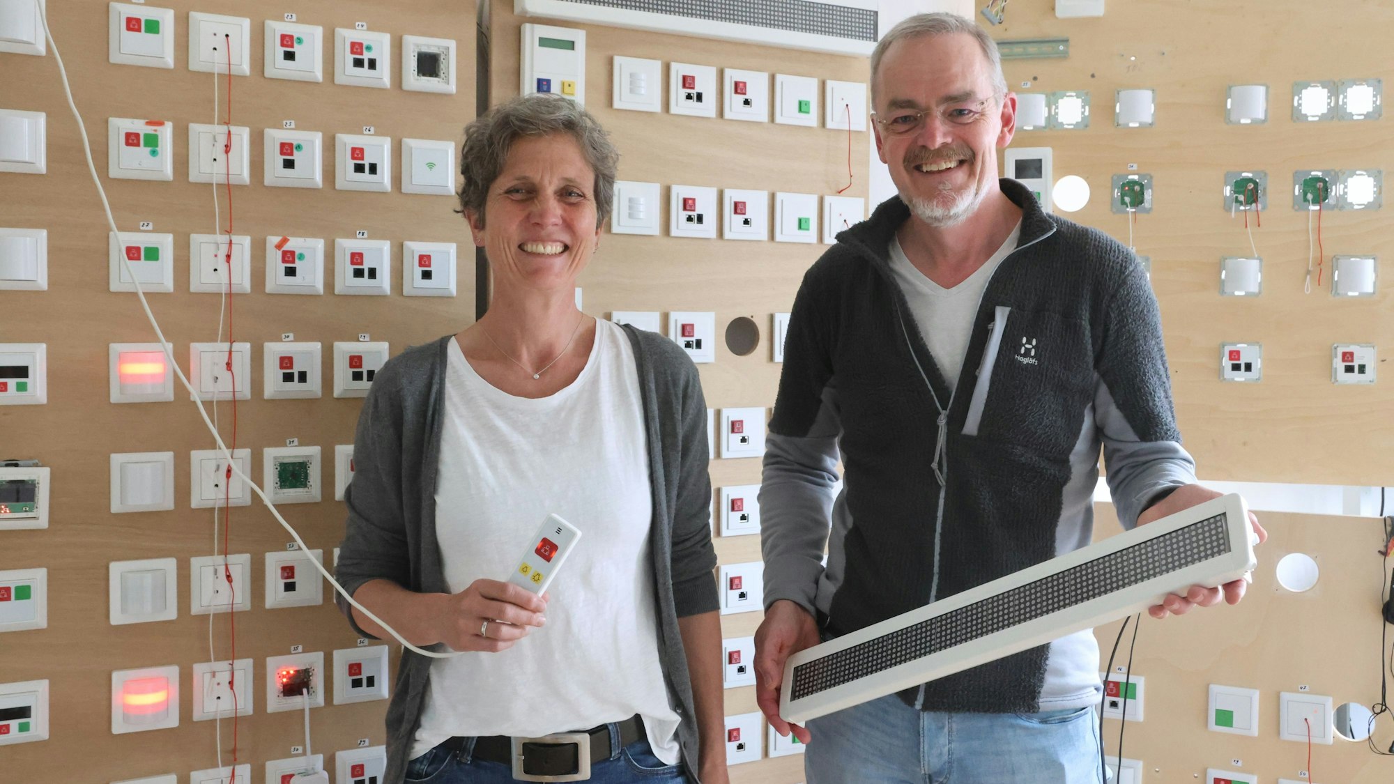 Eine Frau und ein Mann stehen in ihrem Firmenraum und zeigen Rufsysteme für Krankenhäuser und Altenheime.