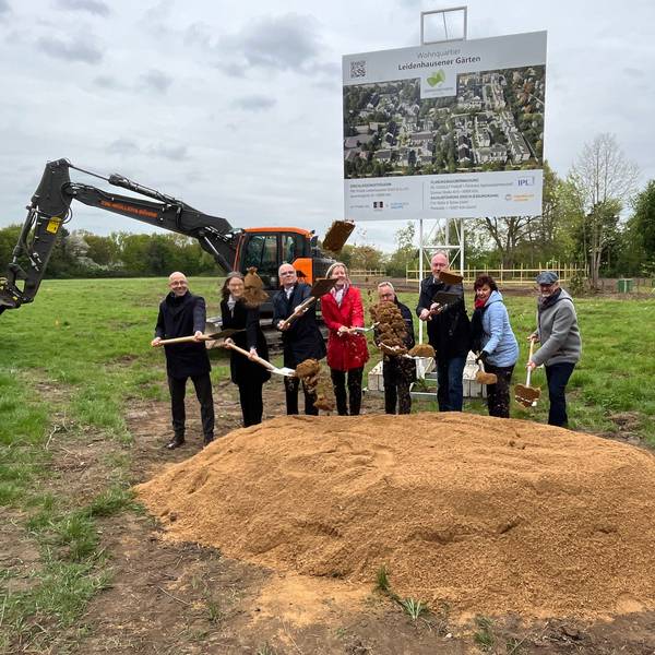 Eine achtköpfige Gruppe hantiert mit Schaufeln an einem Sandhügel auf einer Wiese.