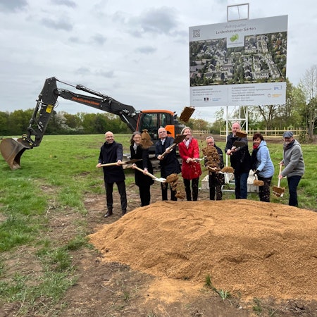 Eine achtköpfige Gruppe hantiert mit Schaufeln an einem Sandhügel auf einer Wiese.