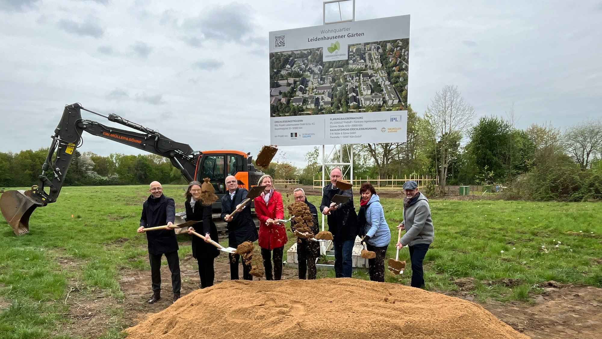 Eine achtköpfige Gruppe hantiert mit Schaufeln an einem Sandhügel auf einer Wiese.