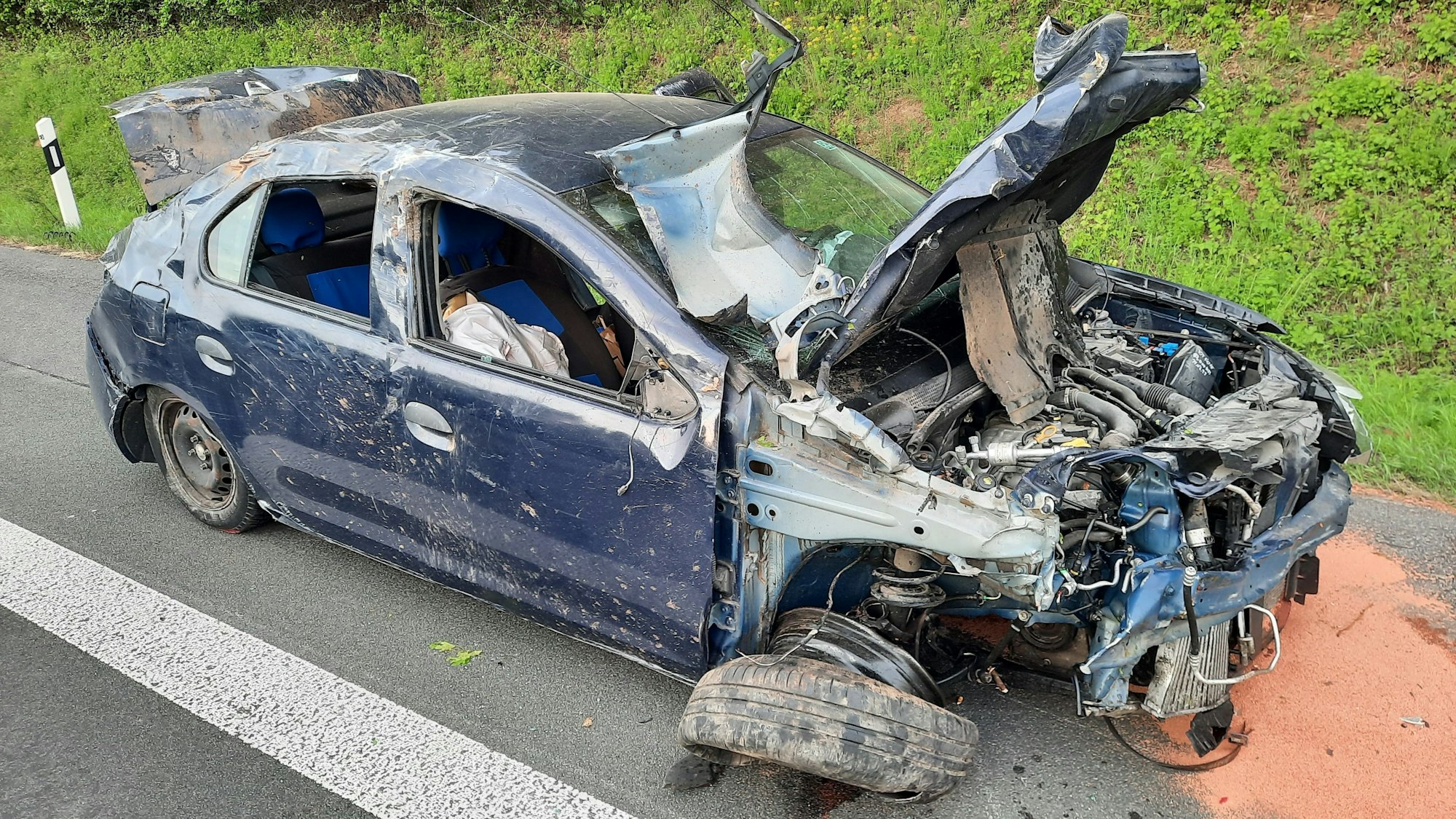 Ein blauer Wagen mit völliger zerstörten Frontpartie, ein Reifen ist fast komplett abgerissen.