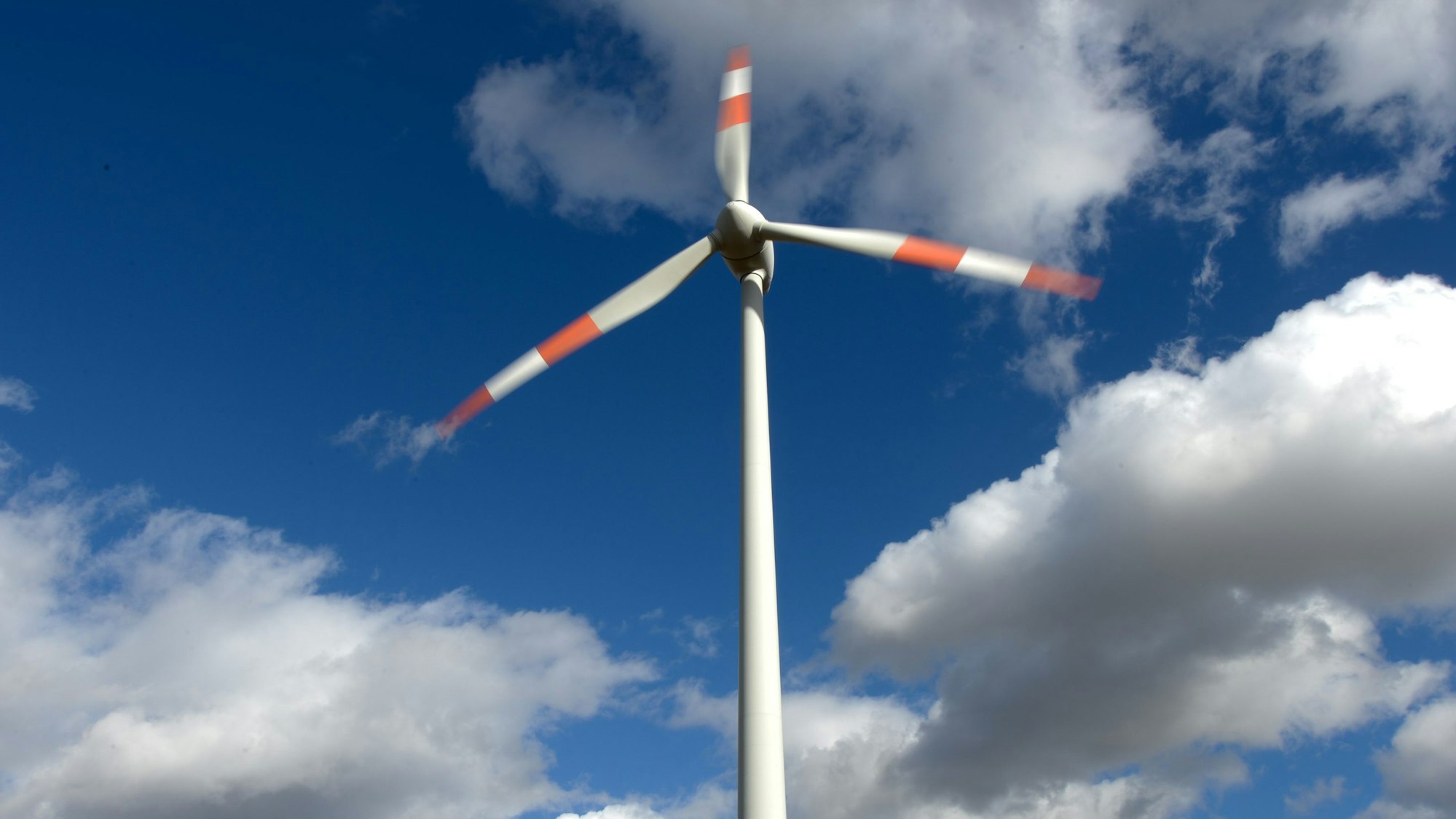 Ein Windrad dreht sich vor weiß-blauem Himmel.