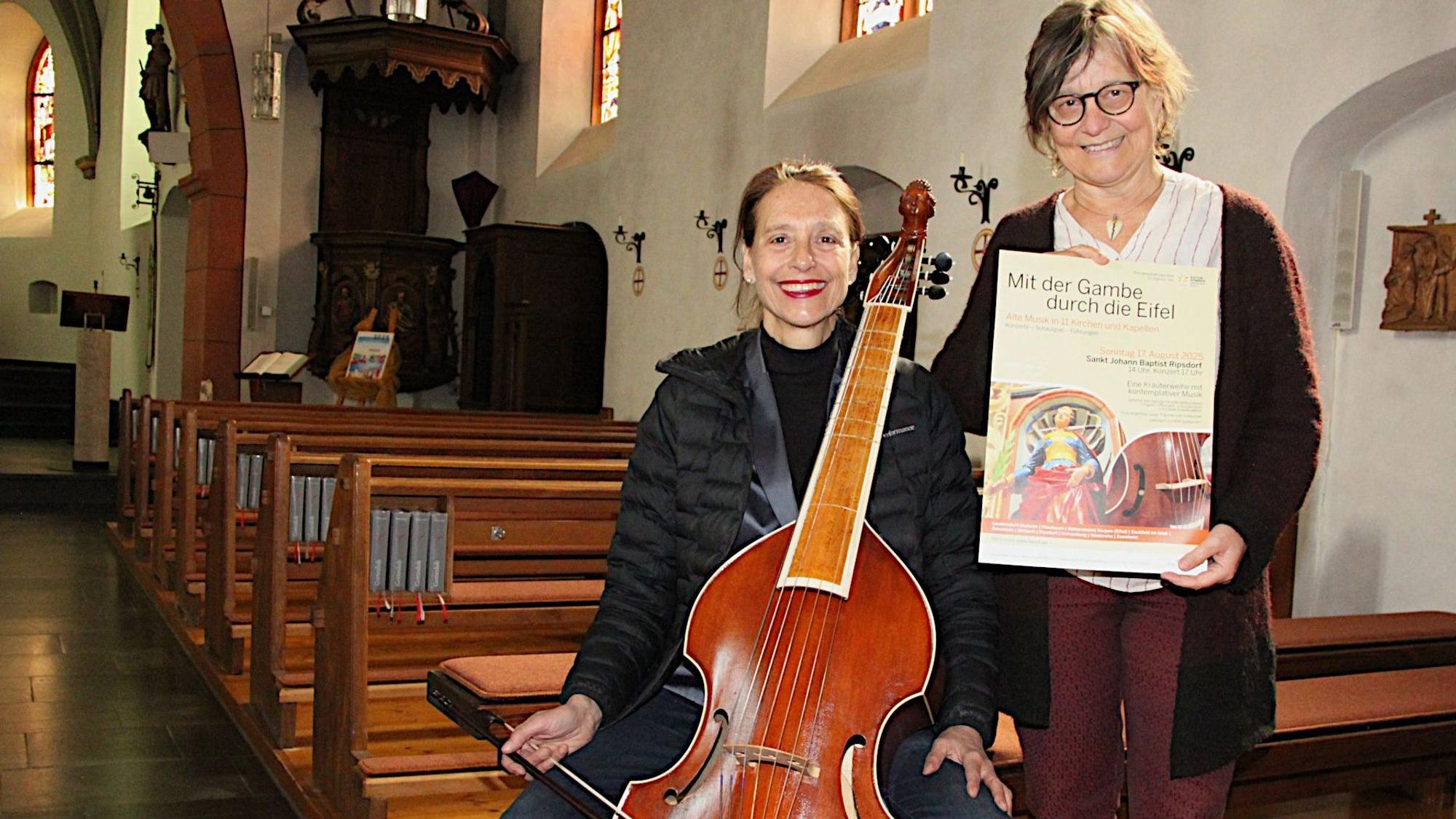 Sabine Weber zeigt eine Gambe, Hildegard Meier das Veranstaltungsplakat.