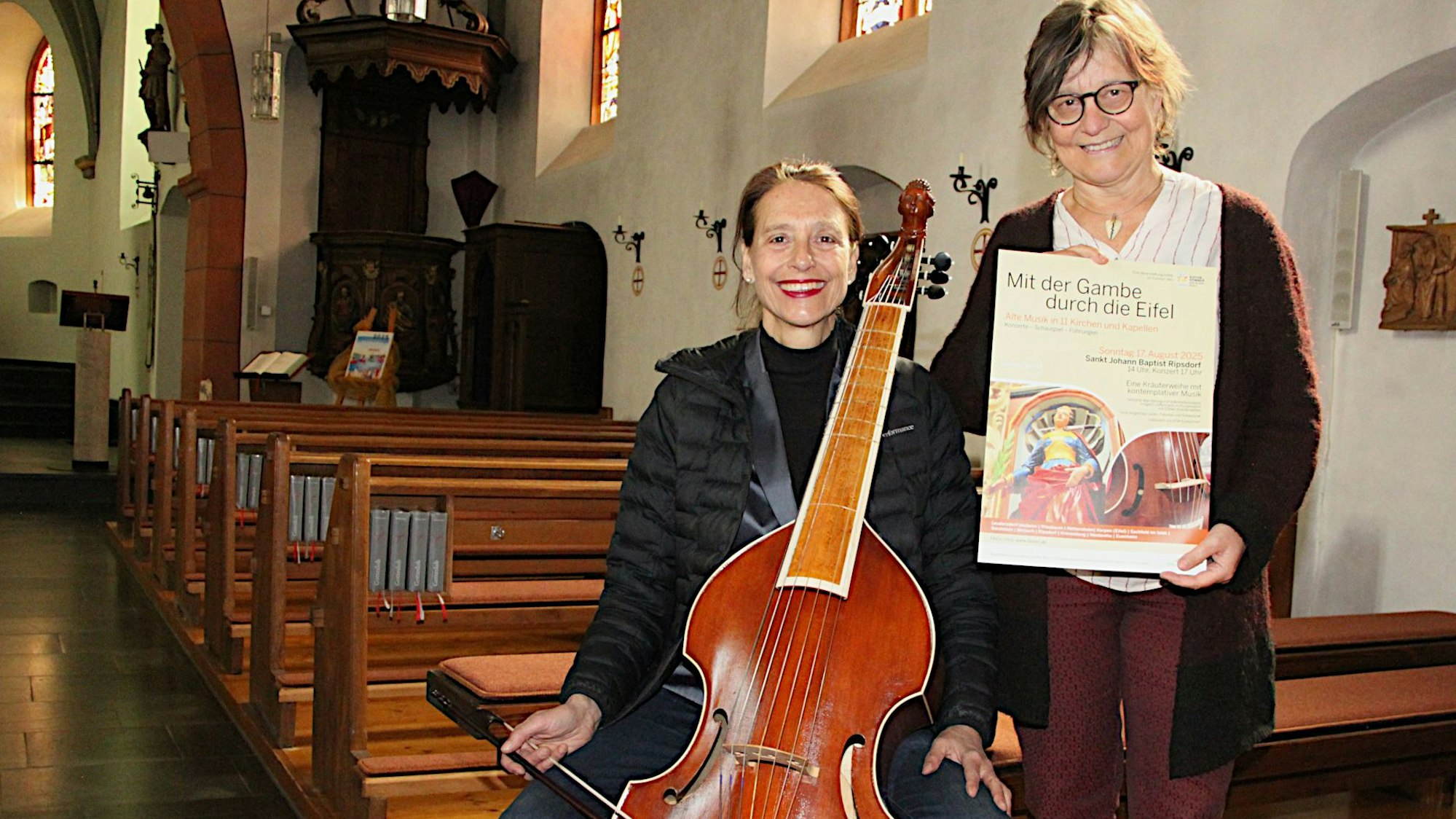 Sabine Weber zeigt eine Gambe, Hildegard Meier das Veranstaltungsplakat.