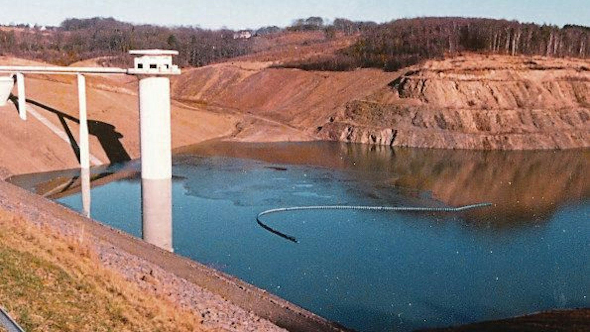 In einer halb aufgestauten Talsperre steht ein Wasserentnahmeturm.