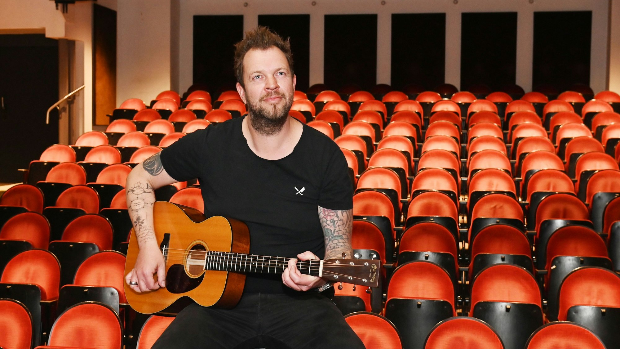 Sven Welter sitzt mit einer Gitarre auf den Stühlen des Theater am Dom.