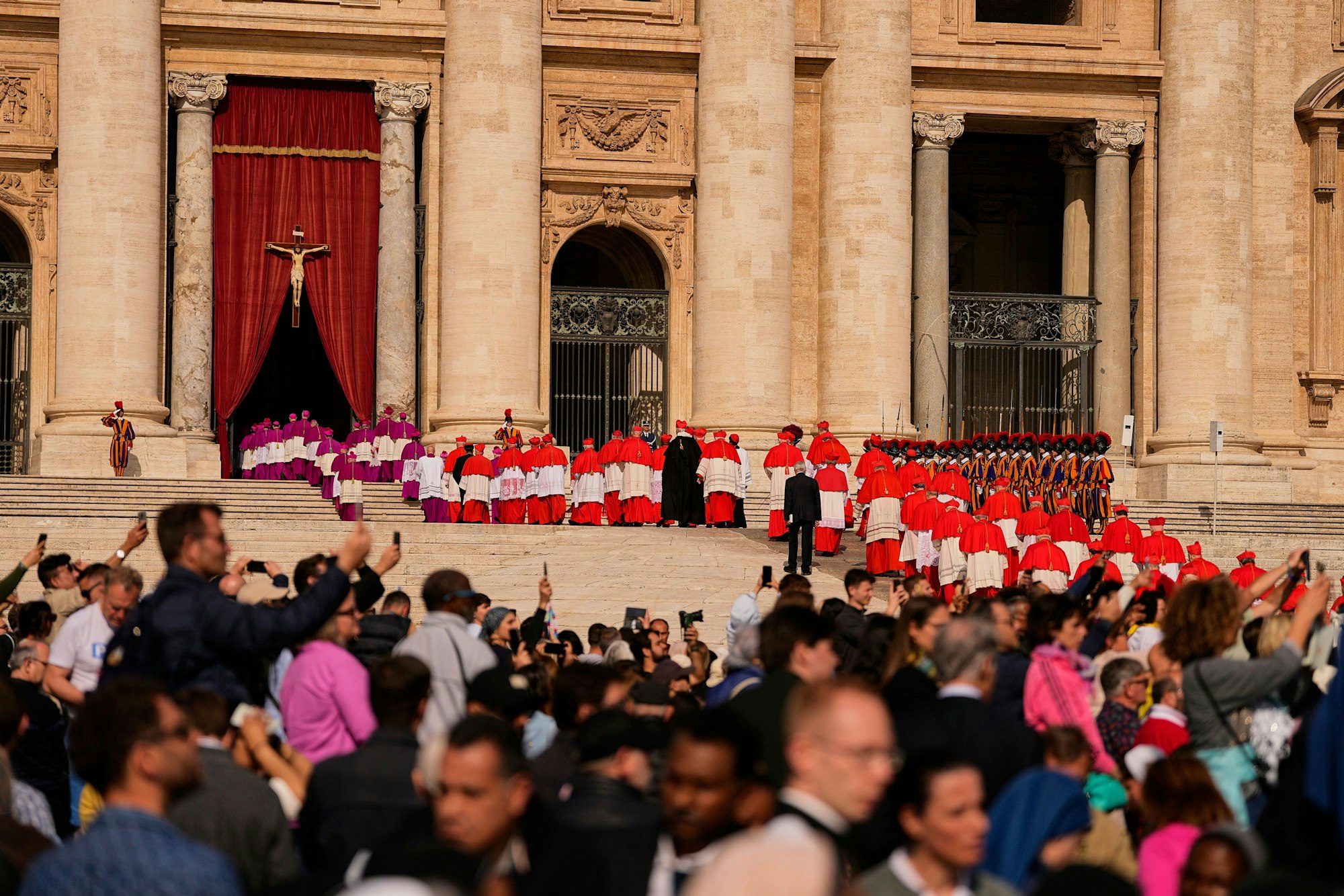 Menschen fotografieren Geistliche, die über den Petersplatz schreiten, bevor der Sarg von Papst Franziskus, der drei Tage lang im Petersdom aufgebahrt sein wird, in den Vatikan gebracht wird.