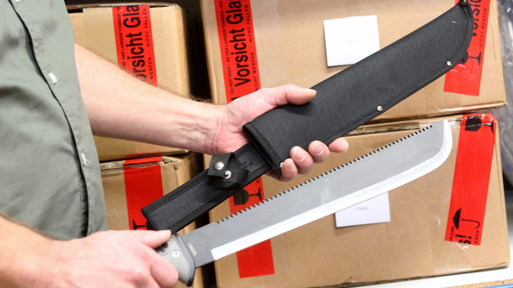 Ein Internethändler führt in seinem Versandkeller eine Machete vor.