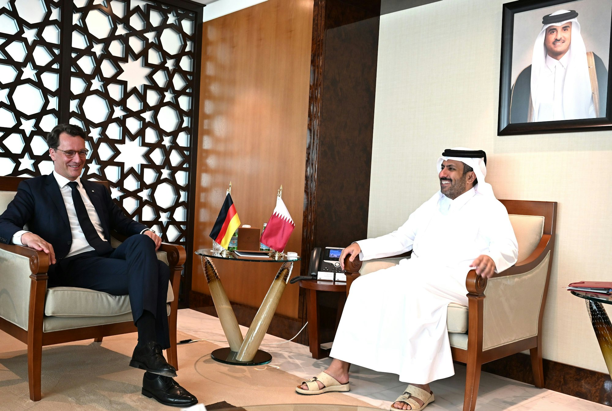 23.04.2025, Katar, Doha: Hendrik Wüst (CDU), Ministerpräsident von Nordrhein-Westfalen, sitzt neben dem Minister für Handel und Industrie von Katar, Scheich Faisal bin Al Thani (r), im Ministerium für Handel und Industrie von Katar. Im Hintergrund ist ein Bild des Emirs von Katar zu sehen, Scheich Tamim bin Hamad bin Khalifa Al Thani. Wüst besucht mit einer Wirtschaftsdelegation Katar und die Vereinigten Arabischen Emirate, um über politische Kooperationen und wirtschaftliche Investitionen zu reden. Foto: Wolf von Dewitz/dpa +++ dpa-Bildfunk +++