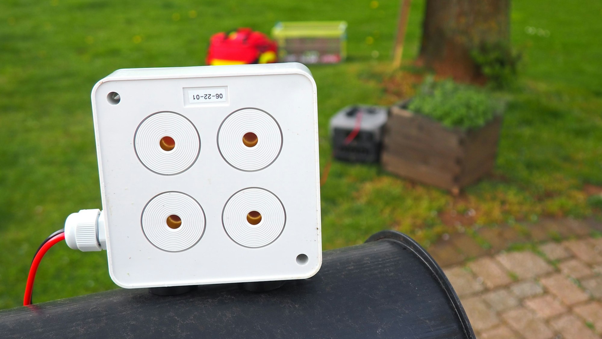 Vor dem Hintergrund einer Wiese ist ein weißes Kästchen zu sehen, das zur Kitzrettung eingesetzt wird, weil es ein durchdringendes Geräusch erzeugt, um  Wild zu vertreiben.