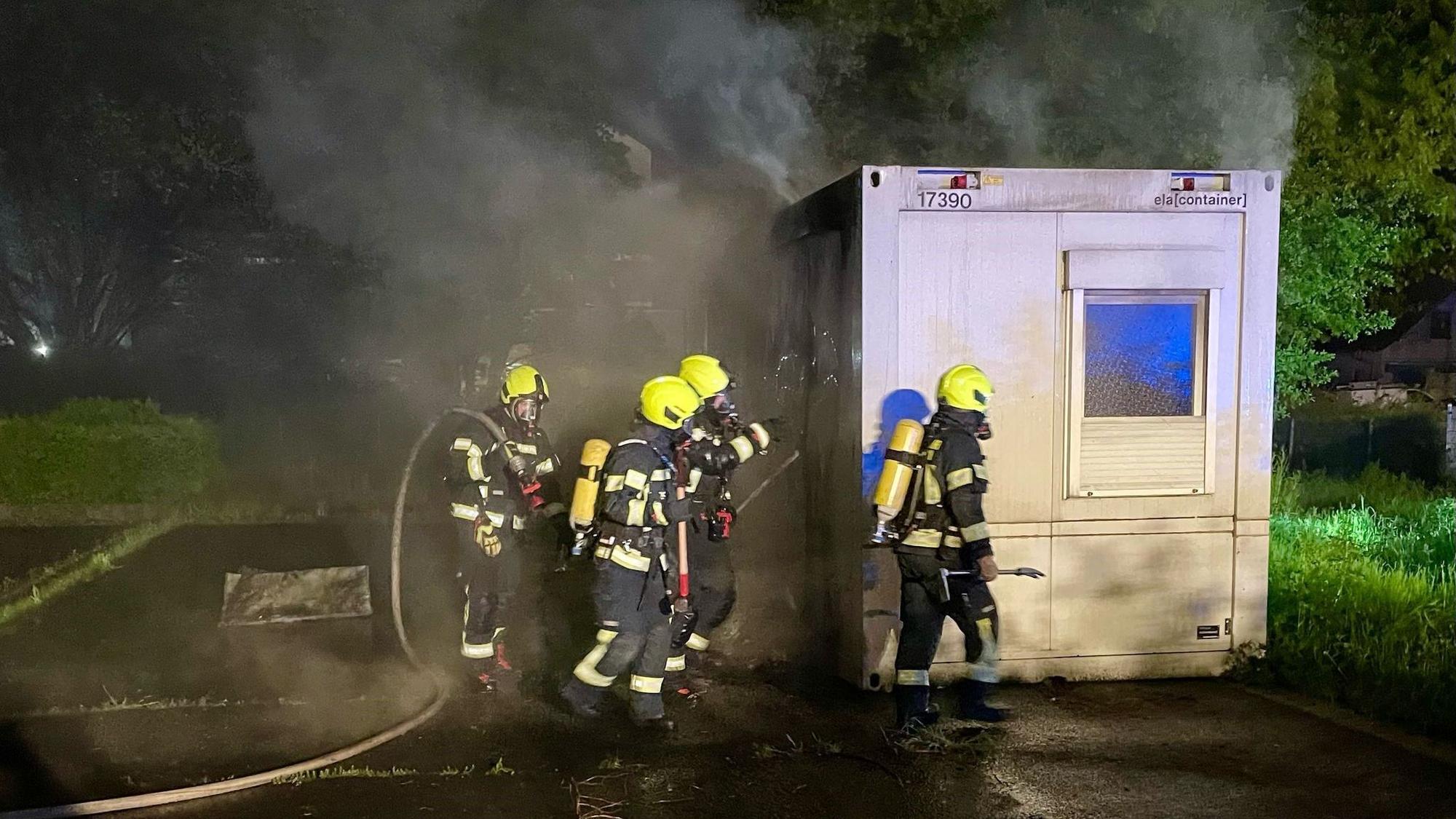 Das Bild zeigt Einsatzkräfte der Feuerwehr an einem qualmenden WC-Container.