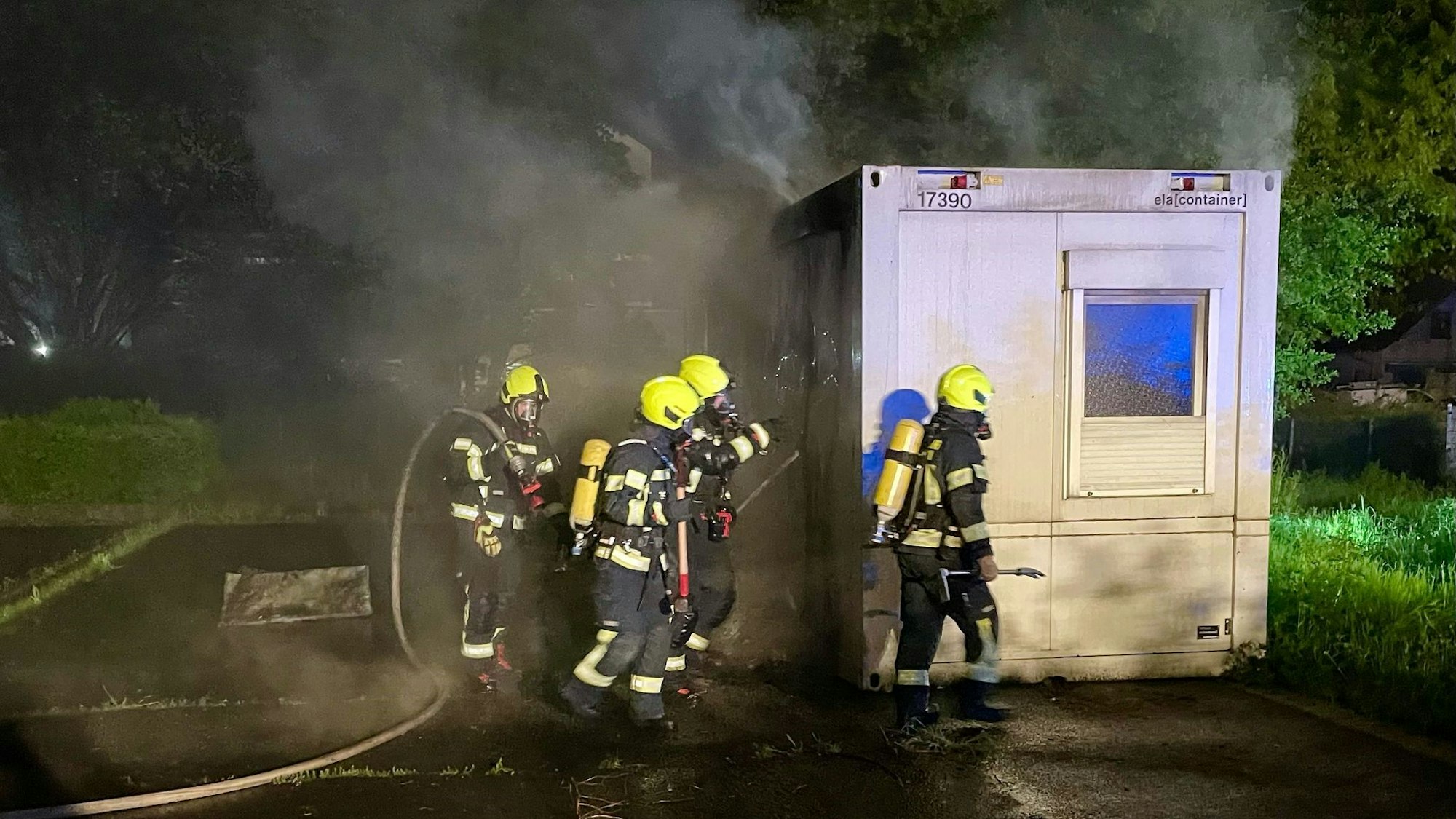 Das Bild zeigt Einsatzkräfte der Feuerwehr an einem qualmenden WC-Container.
