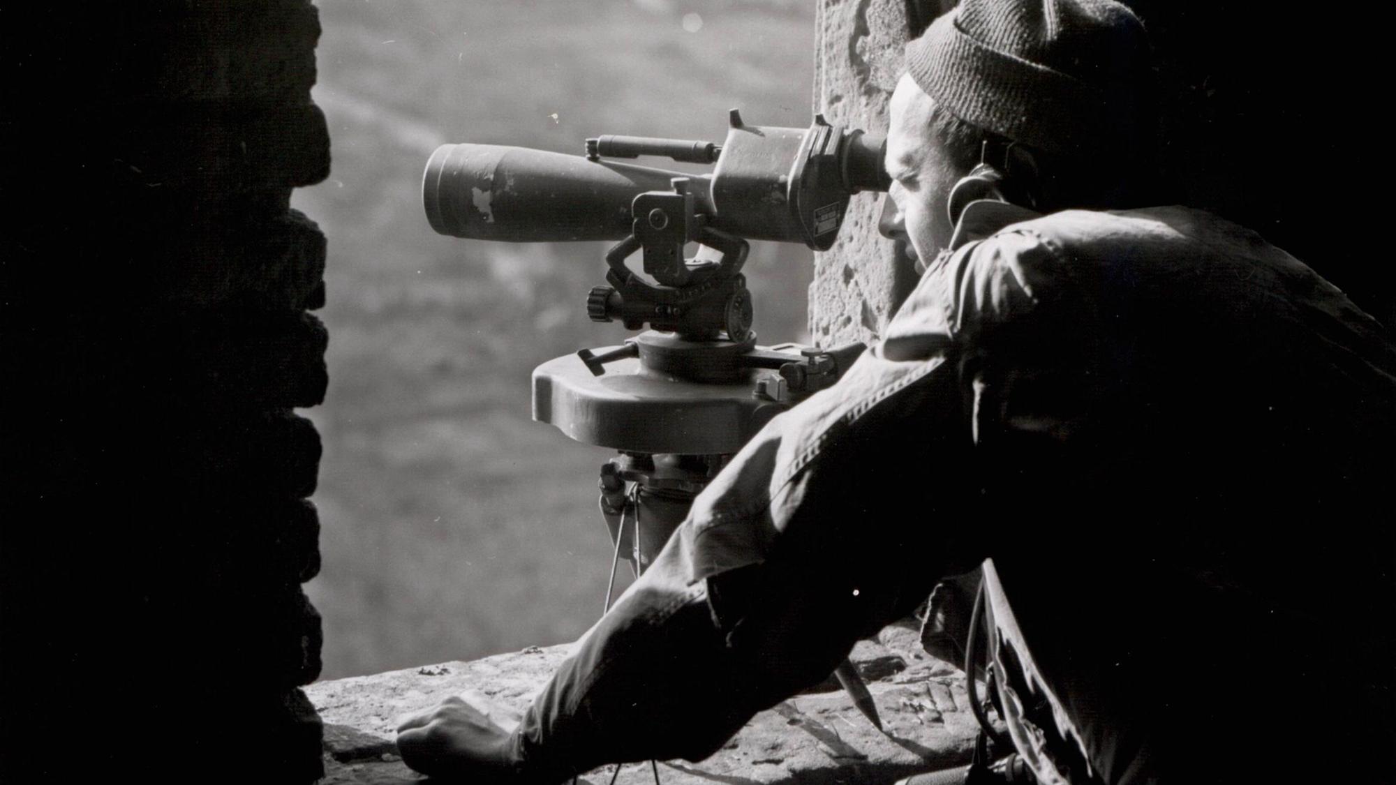 Zu sehen ist auf einem alten Schwarz-Weiß-Foto ein US-Soldat, der mit einem Fernrohr von einem Kirchturm schaut.