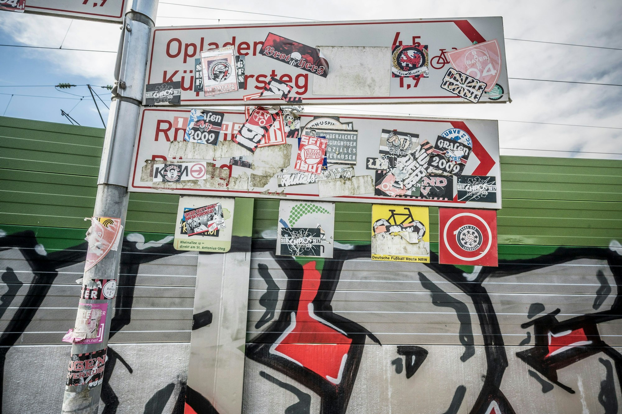 Aufkleber von den Bayer-04- Ultras und anderen auf Fahrrad-Wegweisern im Stadtpark. Foto: Ralf Krieger