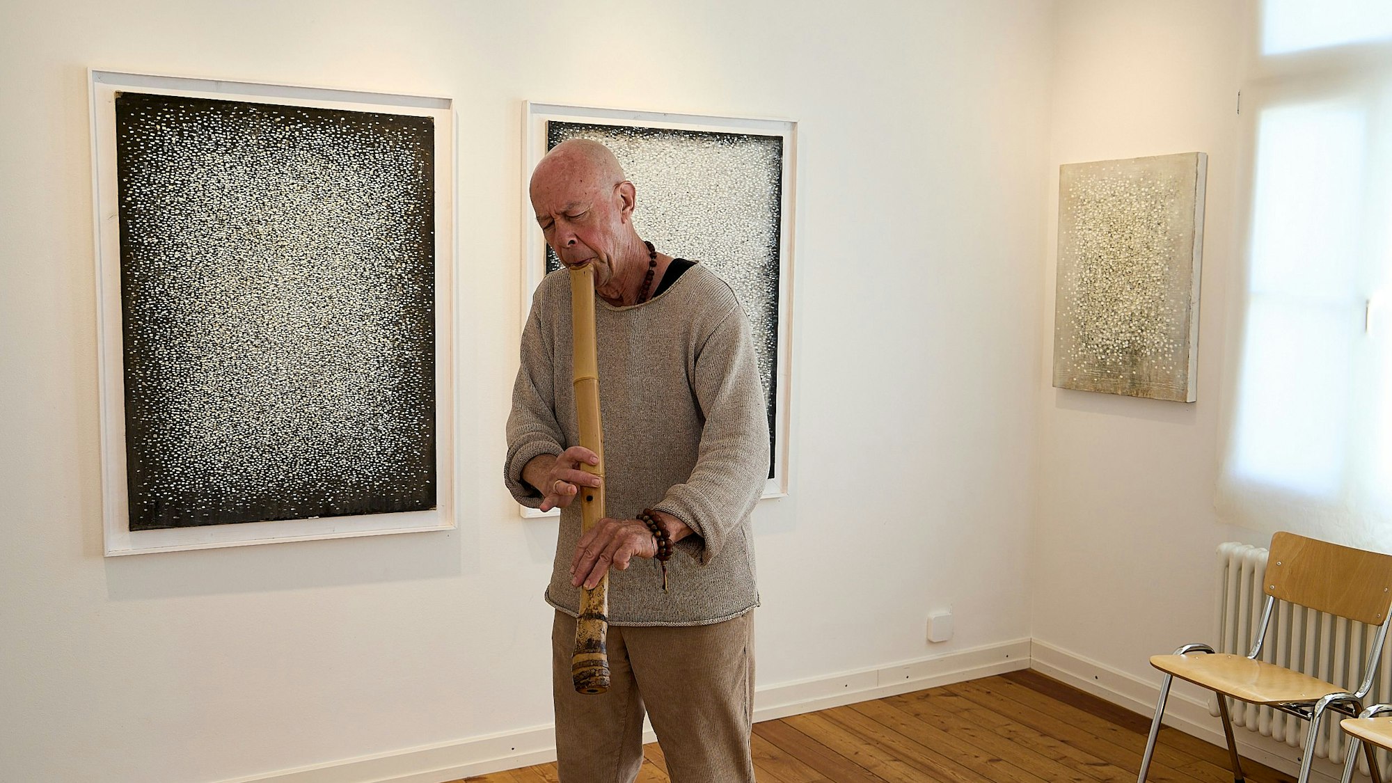 Dan Hepperle steht vor seinen Werken und spielt auf der Shakuhachi, einer Flöte aus Bambusrohr.