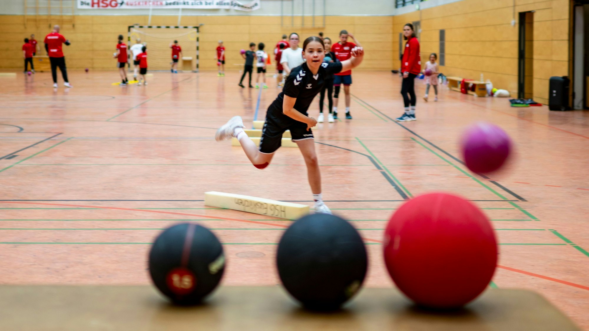 Ein Mädchen versucht, mit einem Ball andere Bälle zu treffen.