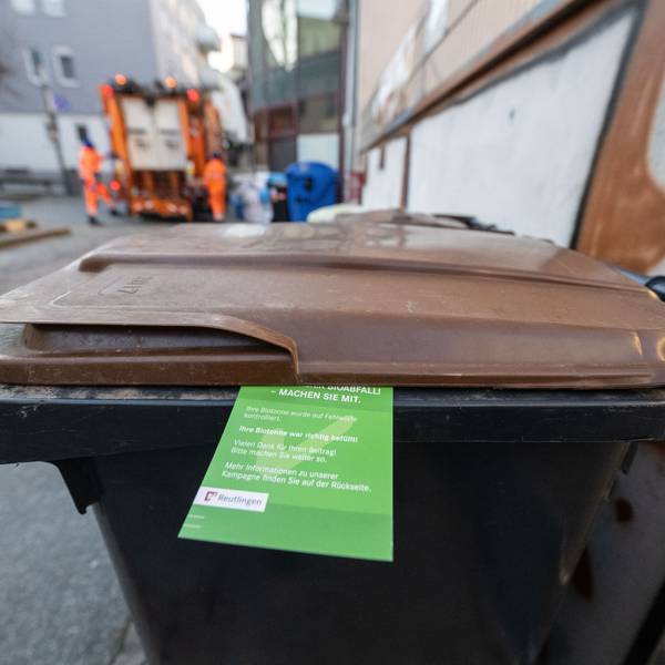 Ein grüner Zettel hängt an einer Biomülltonne.