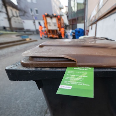 Ein grüner Zettel hängt an einer Biomülltonne.