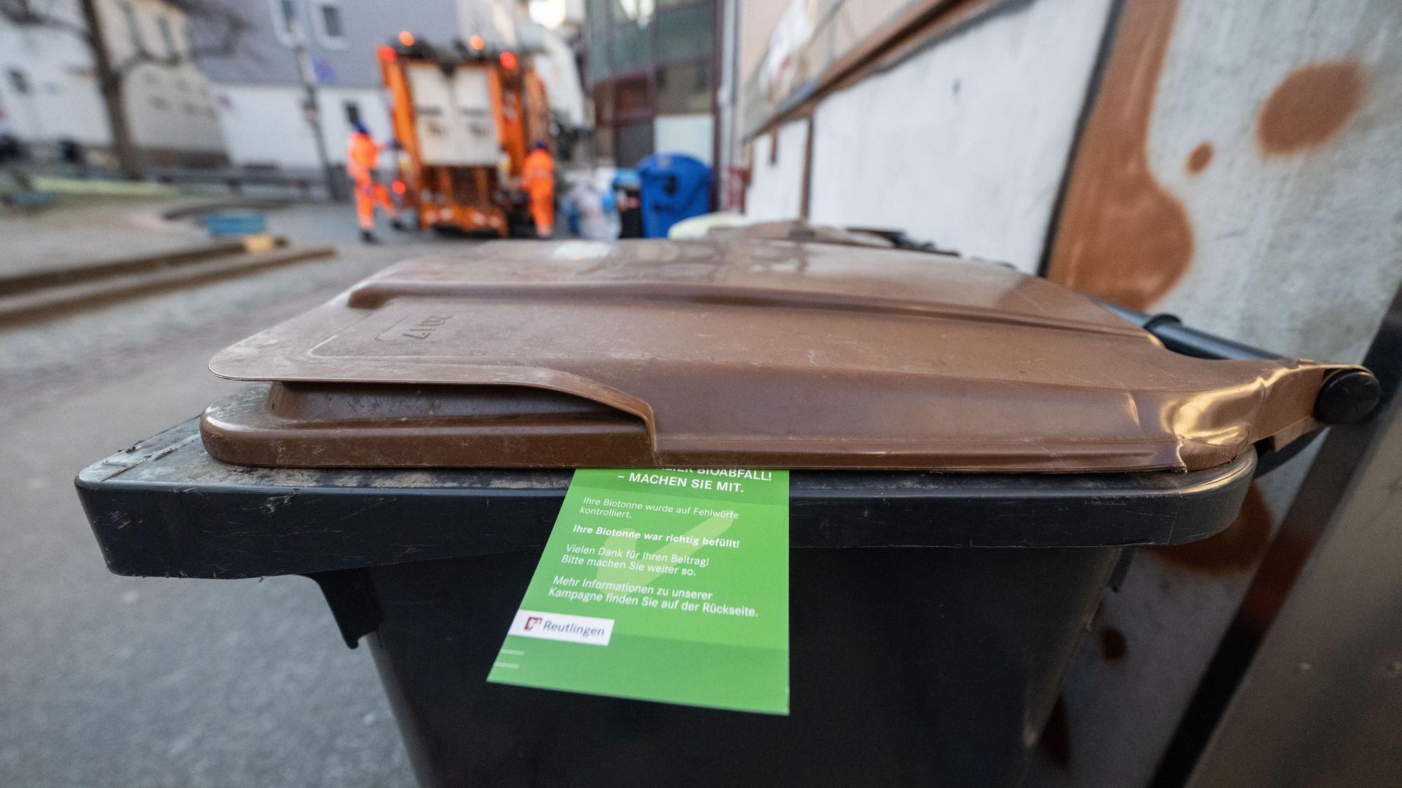 Ein grüner Zettel hängt an einer Biomülltonne.