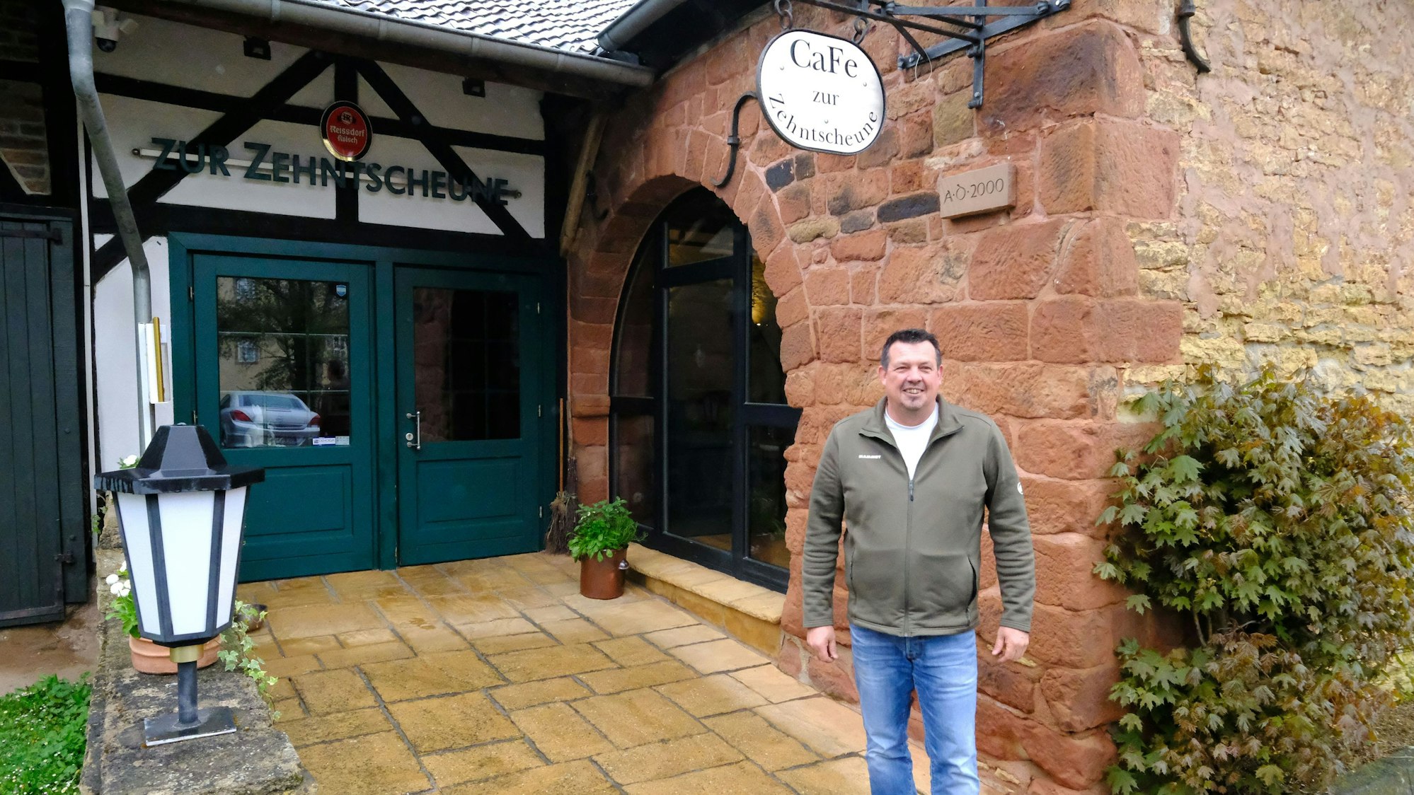 Markus Mathieu steht vor dem Café Zehntscheune in Eicks, das sich in einem historischen Gebäude aus dem Jahr 1613 befindet.