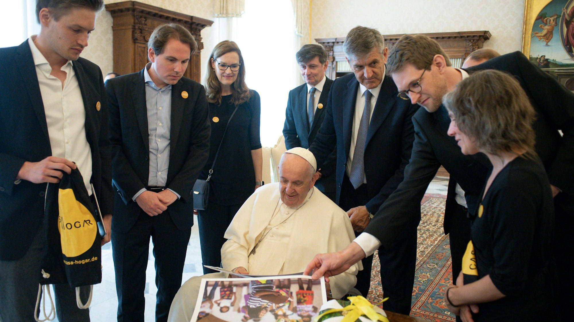 Mehrere Vertreter von Casa Hogar bilden einen Halbkreis um Papst Franziskus, der sich Fotos vom Hilfsprojekt in Kolumbien anschaut.