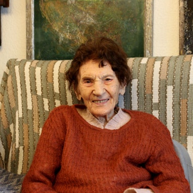 Eine 101-jährige Frau sitzt auf einem Sofa.