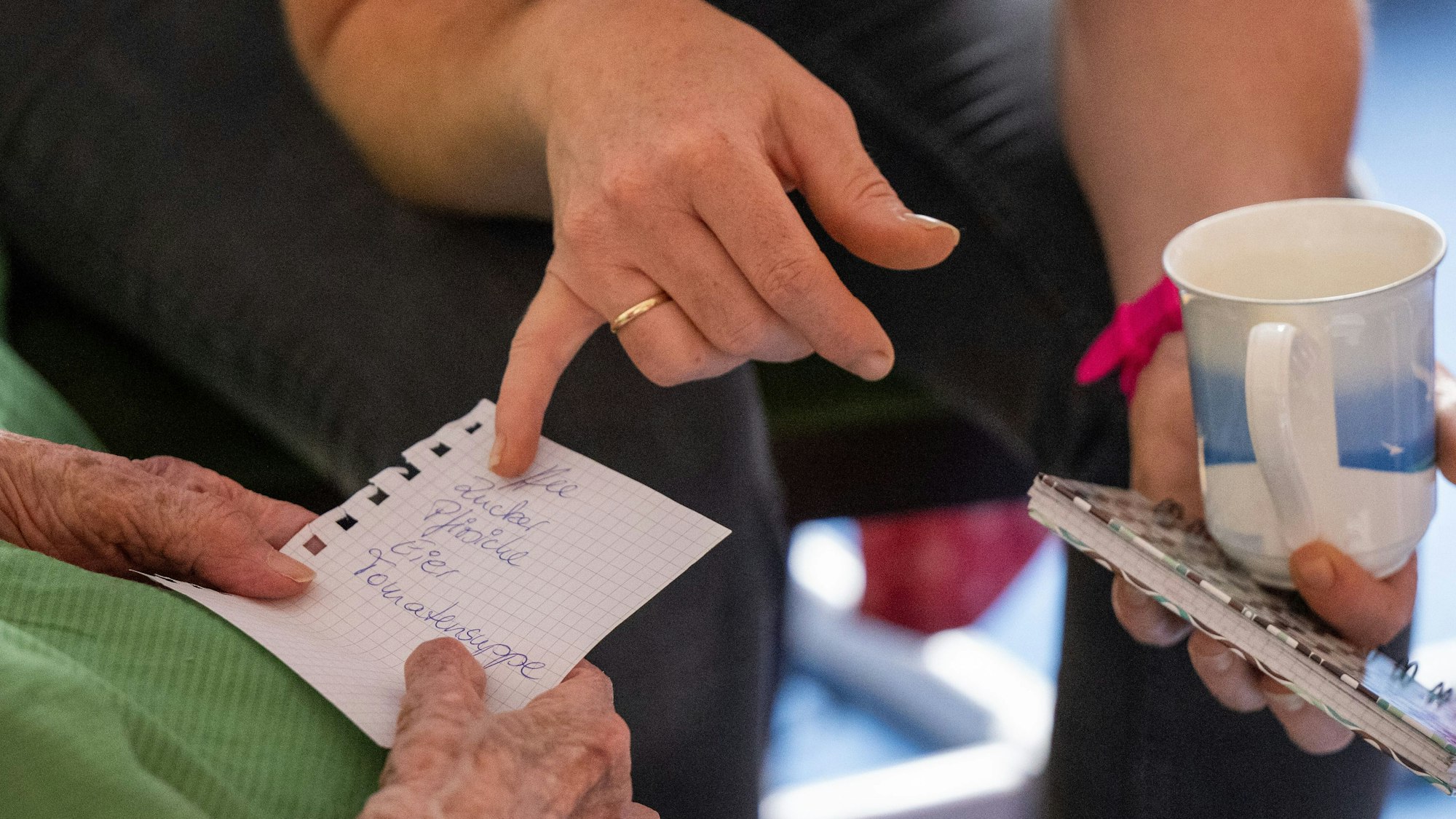 Zu sehen ist eine jüngere Frau, die einer älteren Frau den Einkaufszettel erklärt.