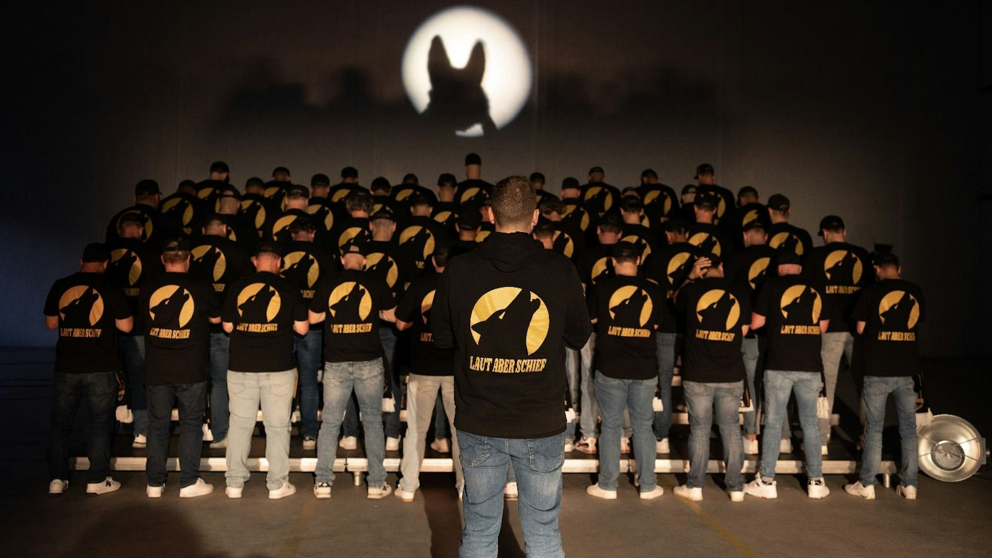 Ein Chor steht mit dem Rücken zur Kamera auf einer Bühne.