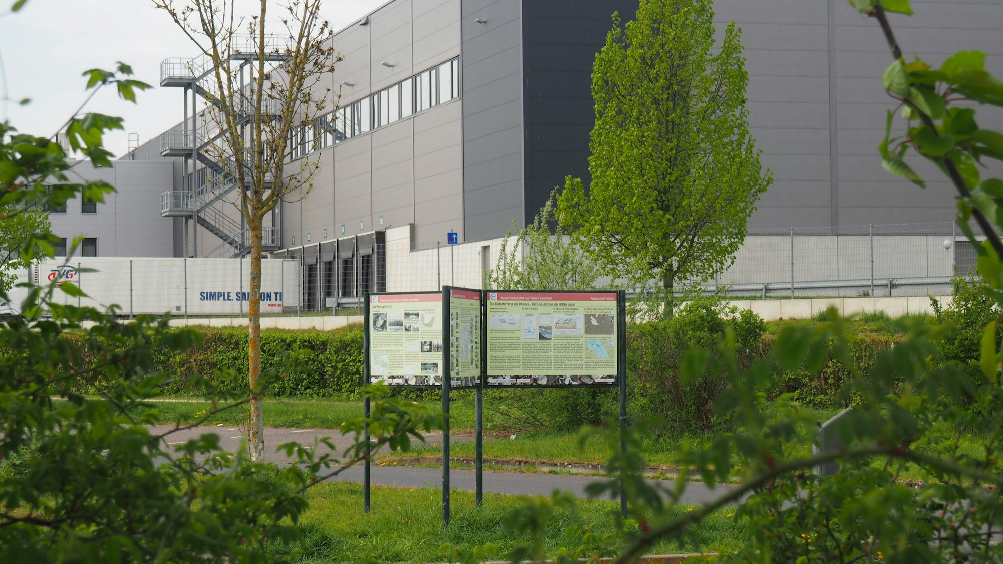 Zu sehen ist ein Gebäude im Hintergrund, davor mehrere Informationstafeln.