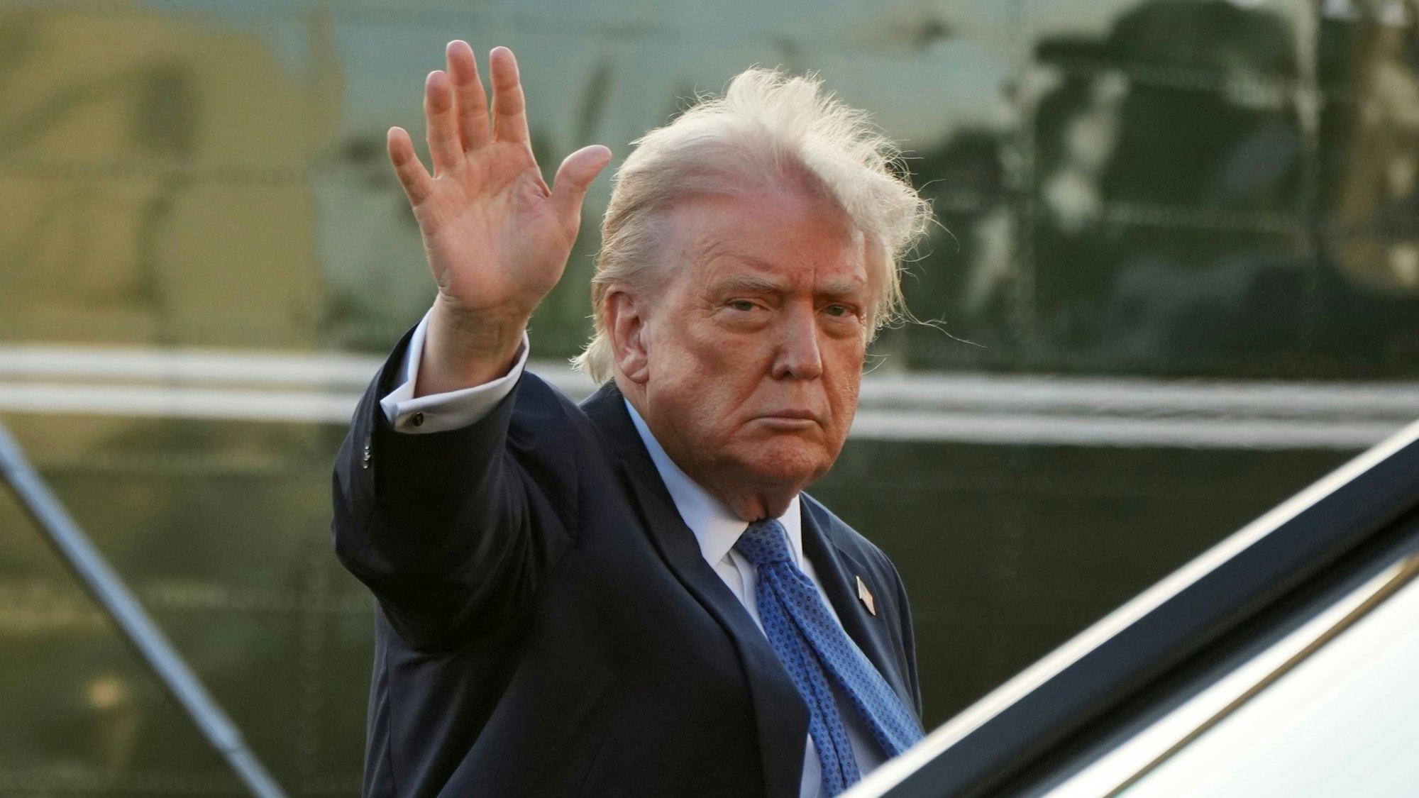 US-Präsident Donald Trump kommt auf einem Flughafen an und winkt mit ernstem Blick in die Kamera.