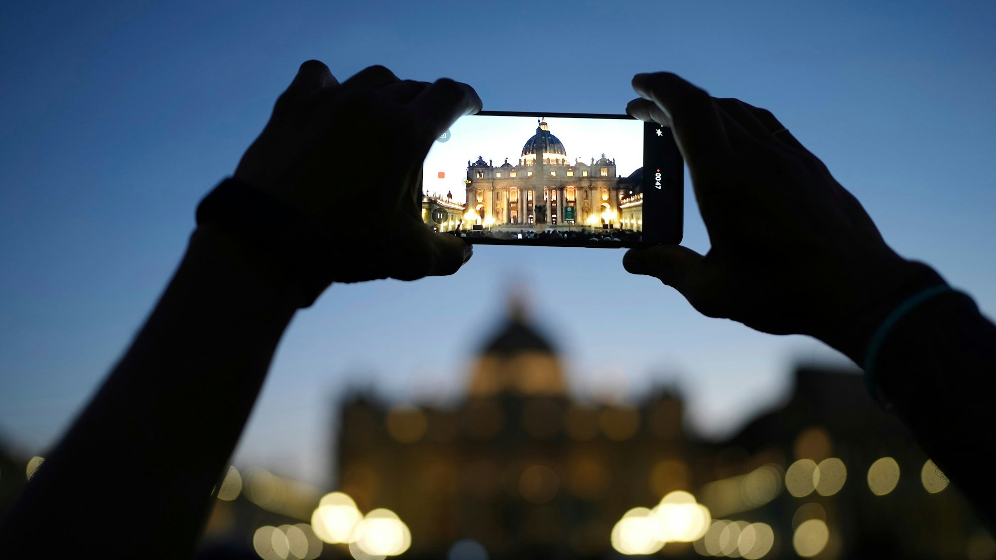 Einer der Gläubigen, die anlässlich des Todes von Papst Franziskus nach Rom gereist sind, macht mit dem Handy ein Foto des Petersdoms.