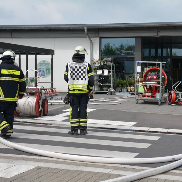 Einsatzkräfte der Feuerwehr mit Schläuchen und einem Großlüfter vor dem Eingang der Aldi-Filiale.