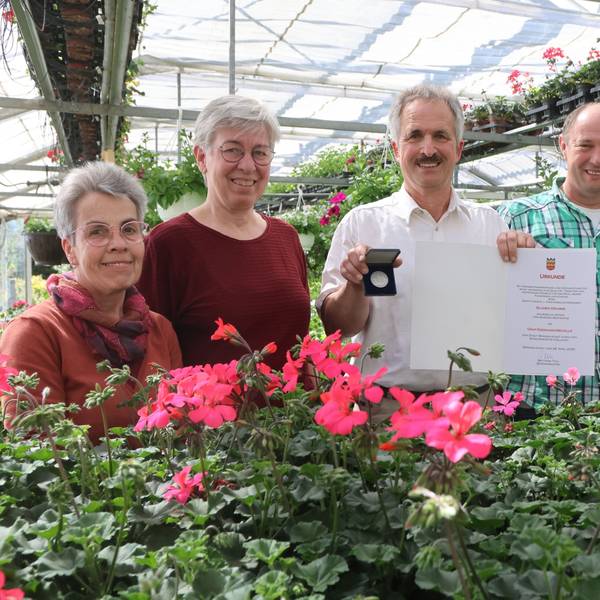 Blumenladeninhaber Jürgen Krumme steht mit seinem Team in der eigenen Gärtnerei. In der Hand hält er eine Medaille und eine Urkunde.