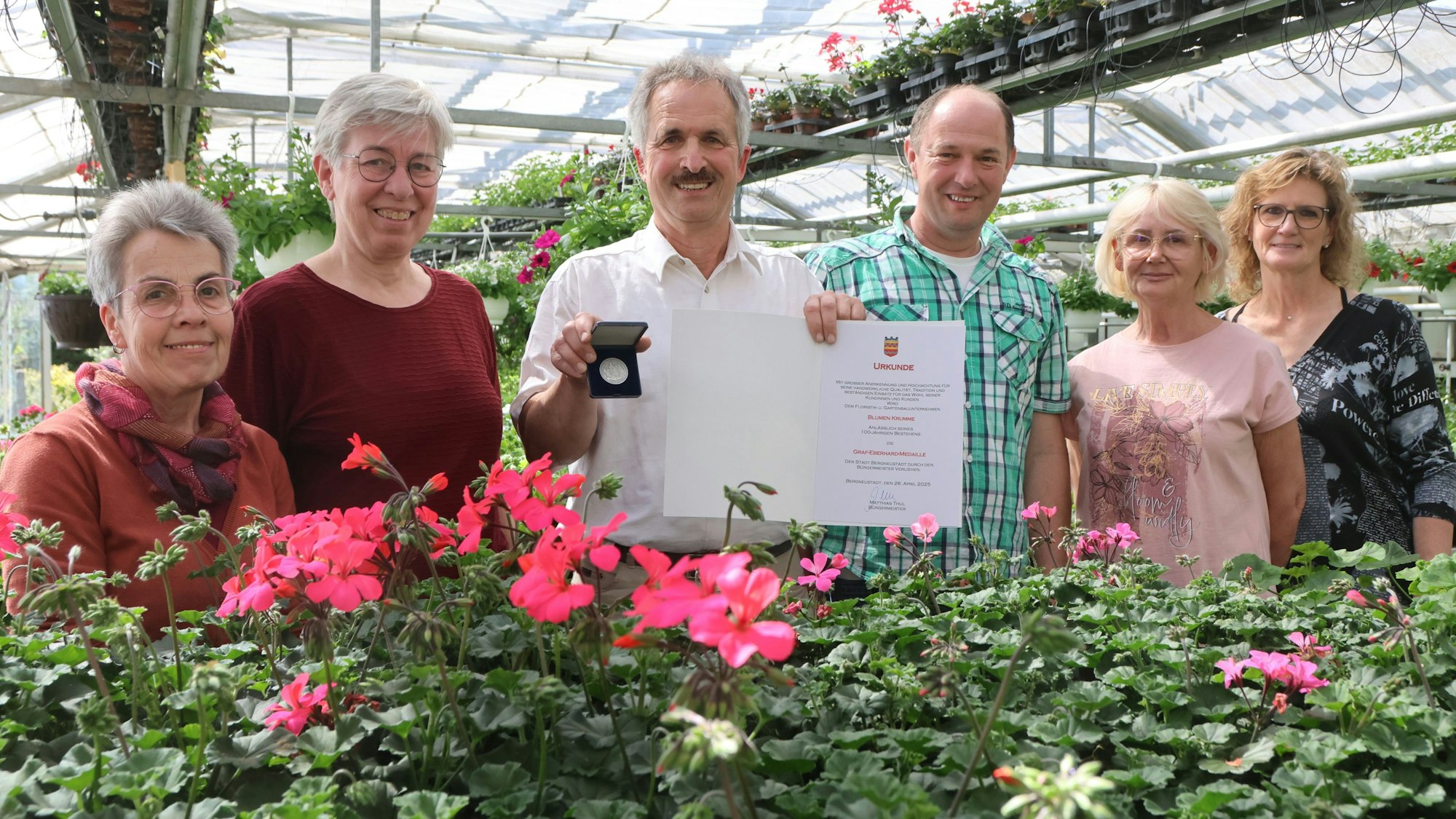 Blumenladeninhaber Jürgen Krumme steht mit seinem Team in der eigenen Gärtnerei. In der Hand hält er eine Medaille und eine Urkunde.